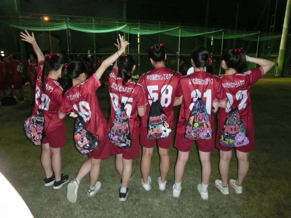 赤いサッカーユニフォーム風のクラスTシャツと、黒のナップサックに可愛く自分の名前や好きなイラストなどでデコり、校庭で写真をとっている女子高生6人の写真